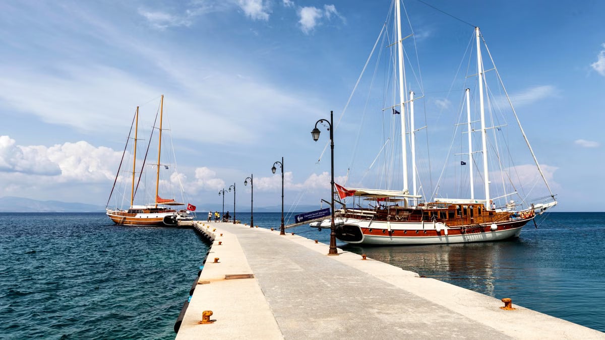 Sailboats moored at a scenic pier in Kos, Greece under a bright summer sky.